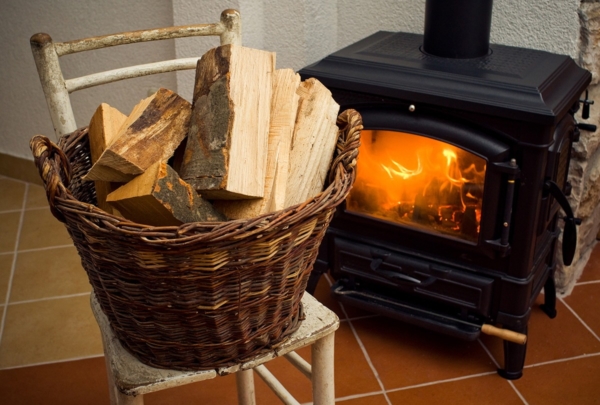 Ein brennender Ofen in einem Wohnzimmer mit Brennholz davor in einem Korb gelagert