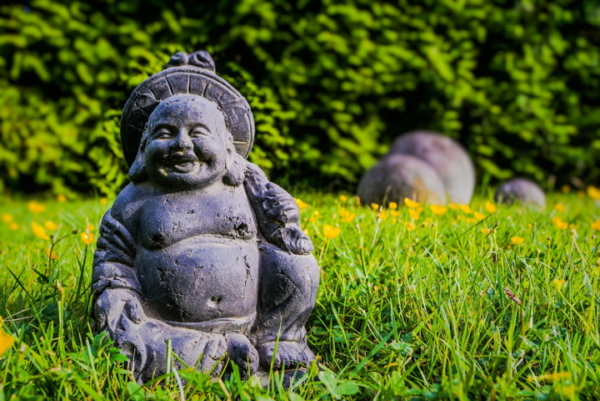 Eine kleine lachende Buddha-Statue steht in einem Garten im Gras