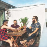 Eine Gruppe junger Menschen sitzt am Balkon an einem Tisch und lacht