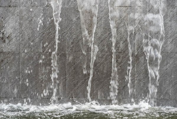 An einer Betonwand fällt Wasser in Form eines Wasserfalls herunter