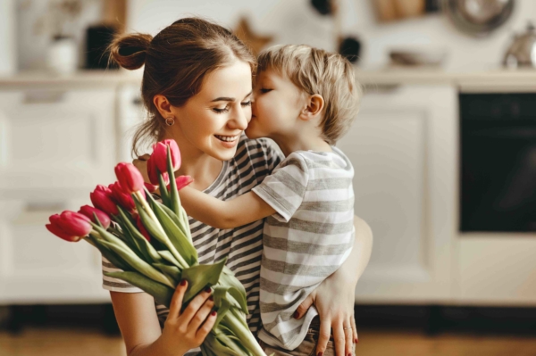 Sohn umarmt Mutter und gibt ihr einen Kuss auf die Wange, sie hält rote Tulpen in der Hand