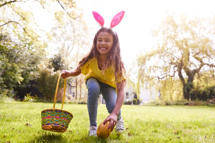 Ein Mädchen hebt gerade ein Osterei vom Boden auf und hält in der anderen Hand ein Osterkorb