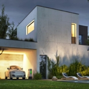 Man sieht ein modernes Haus mit einem e-Auto und einer e- Ladestation unter einem Carport