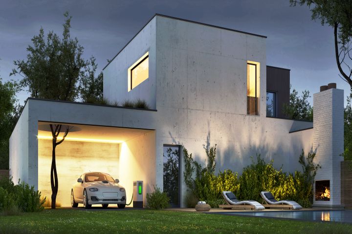 Man sieht ein modernes Haus mit einem e-Auto und einer e- Ladestation unter einem Carport