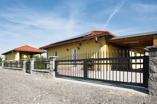 Zweiflügeltor konvex rund mit Dekorringen und Lanze in anthrazit, Modell Venezia, in grauer Steinmauer vor gelbem Haus