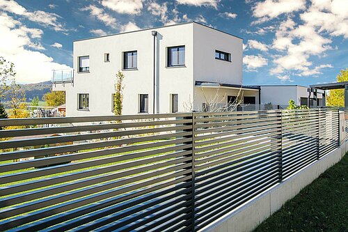 Man sieht einen Lamellenzaun in anthrazit, Modell Linea von GUARDI, Gewinner-Zaun des Infinity Design Award, vor einem weißen, modernen Haus