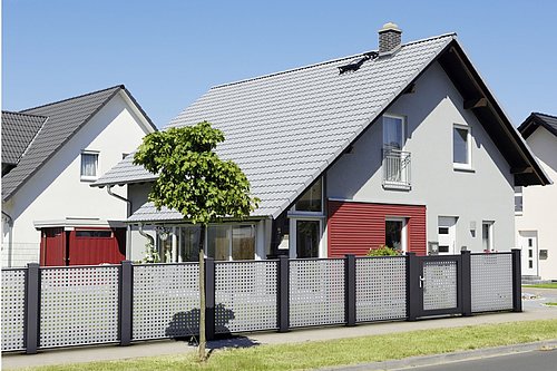 Architektonischer Lochblechzaun in grau mit schwarzen Stehern, mit passender Gehtür, Modell Loos von GUARDI, vor grauem Haus 