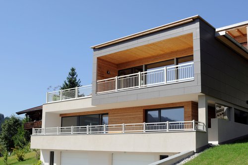 Balkon aus Einzelstäben in weiß, Modell Toskana, auf einem modernen, grauen Haus mit Holzelementen