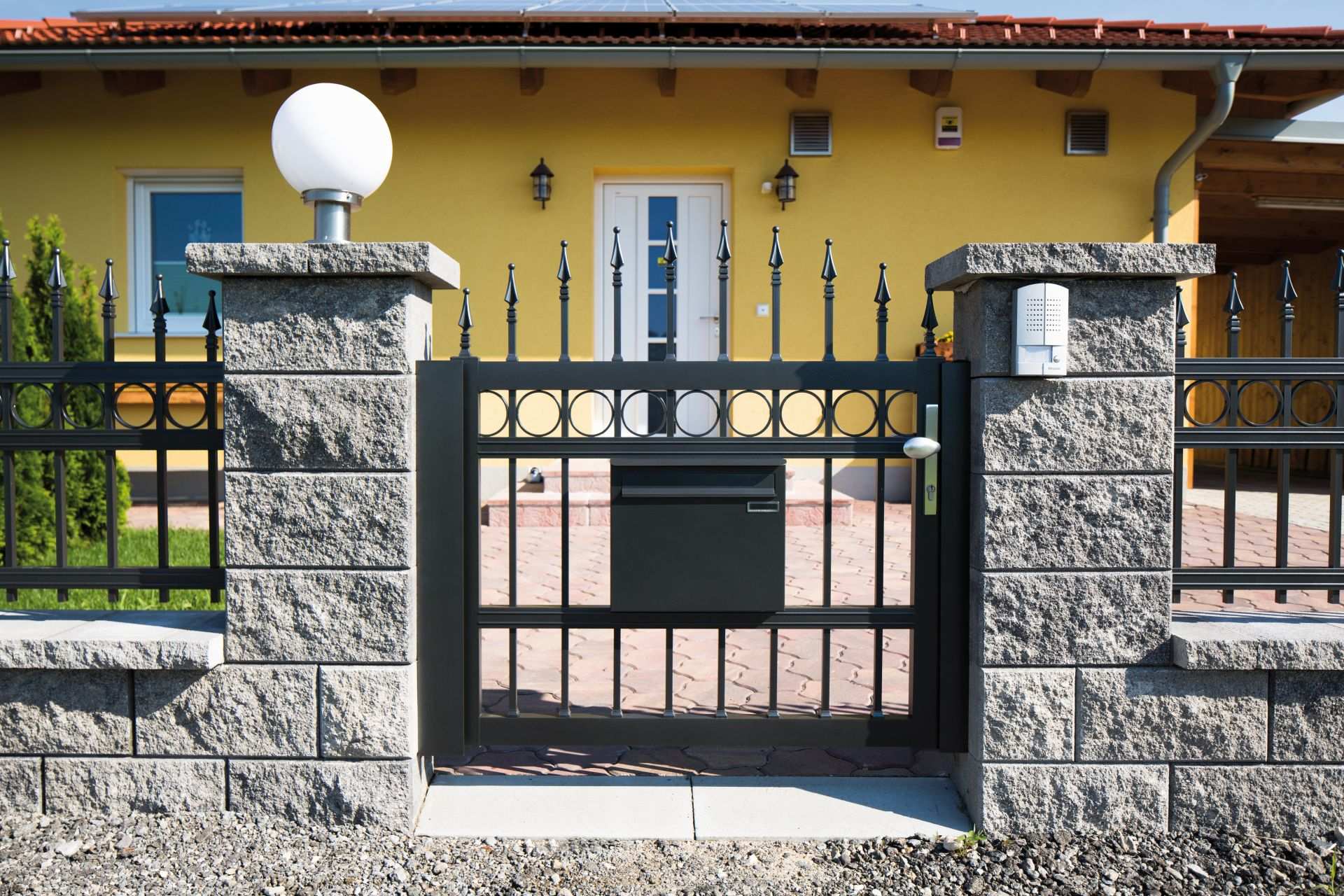 Gartentüre konvex in anthrazit mit Dekorringen und Lanze, mit passendem Briefkasten, Modell Venezia, vor gelbem Haus in Steinmauer integriert