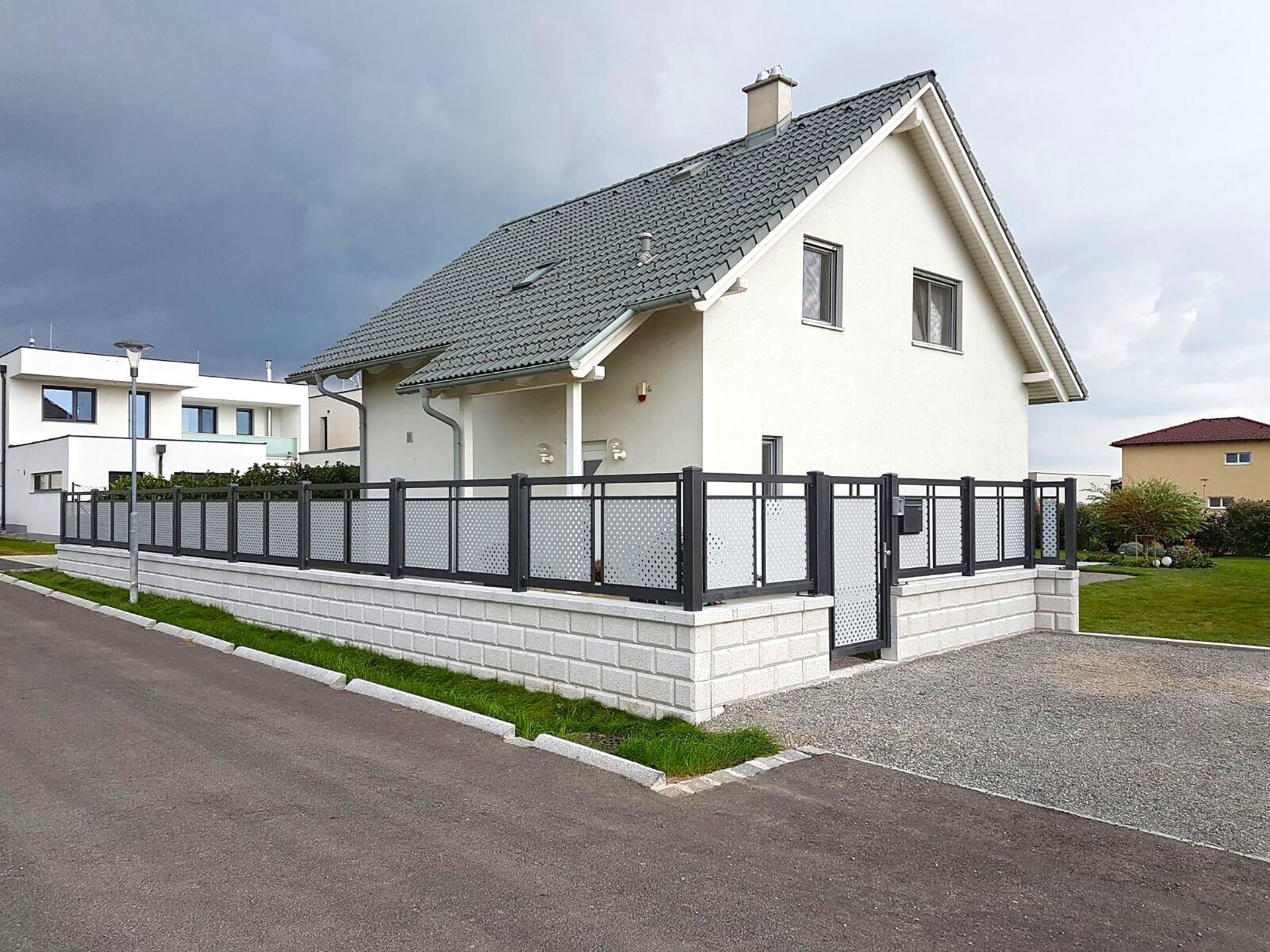 Dekorzaun in anthrazit mit grauer Lochblechfüllung, mit passender Gartentüre, Modell Loskana von GUARDI, vor weißem Einfamilienhaus