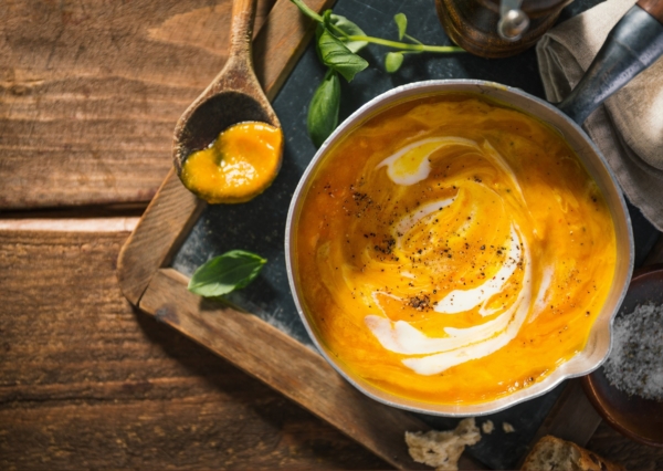 Kürbiscremesuppe in einer runden Schüssel serviert auf einem Holzbrett