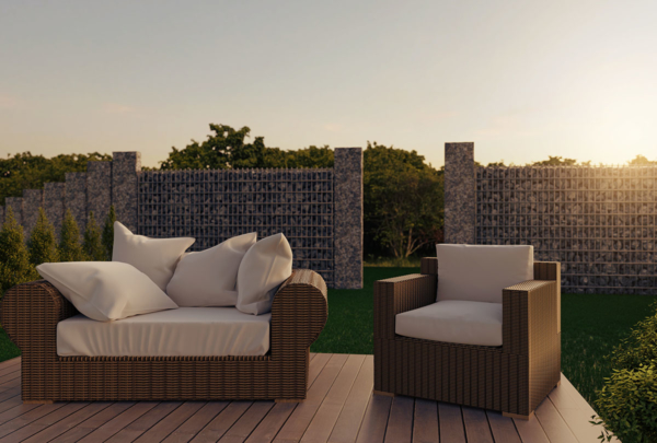 Eine Gartengarnitur aus Rattan steht auf einer Terrasse, im Hintergrund ein Gabionenzaun
