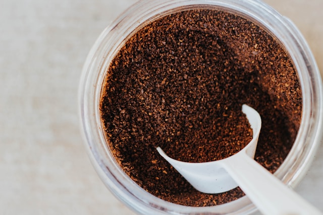 Kaffeesatz mit weißem Messlöffel im Glascontainer